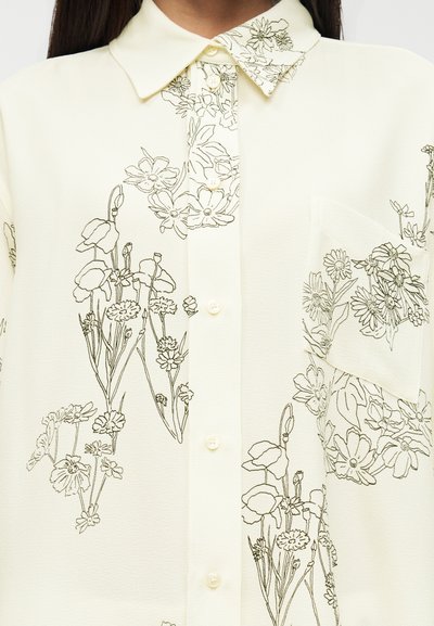 Ανοιχτό κίτρινο μπλούζα με σχεδιασμούς λουλουδιών σε γραμμή, με μυτερό γιακά, κλείσιμο με κουμπιά και τσέπη στο στήθος. Ομαλή, ελαφριά υφή υφάσματος.