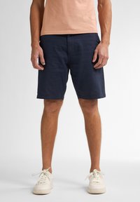 Shorts azul marino en un diseño casual, con una textura suave, bolsillos laterales y un ajuste relajado. Combinados con una camiseta de melocotón claro.