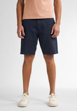 Pantaloni scurți de culoare albastru marin, cu un design casual, având o textură netedă, buzunare laterale și o croială lejeră. Asortați cu un tricou de culoare piersică deschisă.