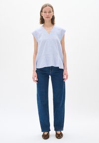 Modrá a biela pruhovaná blúzka s výstrihom do V, krátkymi rukávmi a rozšírenou siluetou, kombinovaná s rovnými tmavými džínsami a balerínkami s potlačou zvierat.