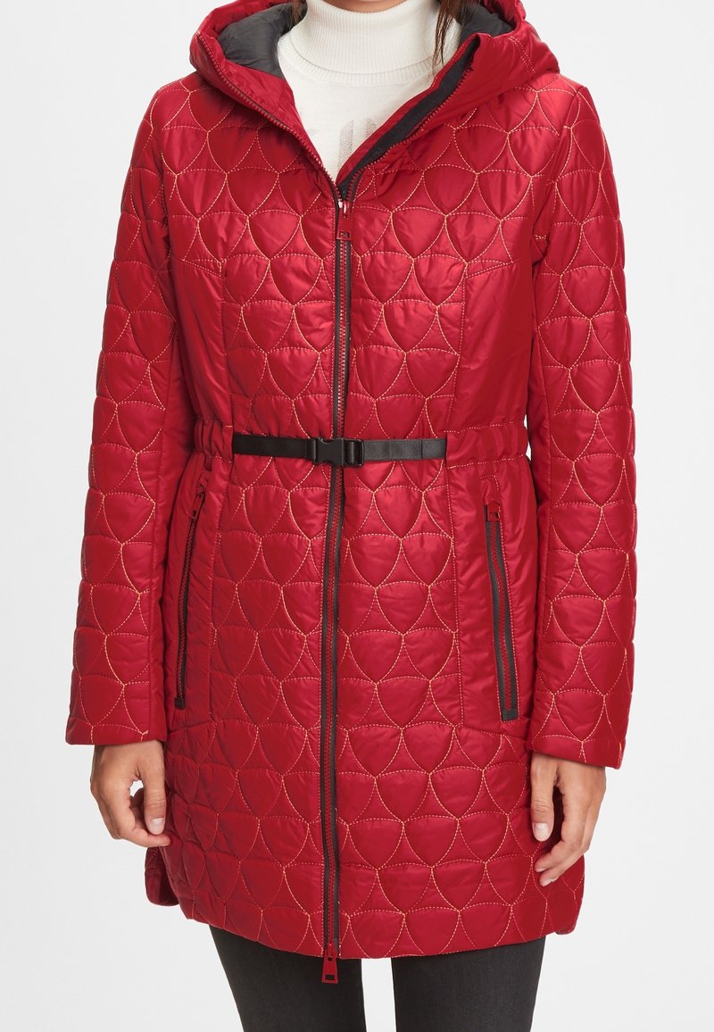Rød quilted frakke med hætte, der har en bælte, lynlåslommer og et tekstureret mønster af overlappende former. Sorte accenter fremhæver detaljer.