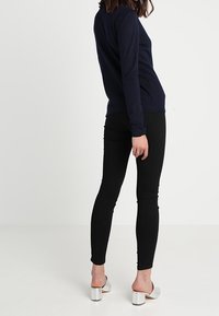 Marinblå långärmad topp, åtsittande svarta leggings och metalliskt silverfärgade mule-skor med klack. Toppen har en enkel design och leggingsen är stretchiga.