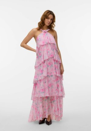 Frau trägt ein mehrlagiges, rosa Maxikleid mit Blumenmuster und Neckholder, aus fließendem Chiffonstoff, dazu schwarze spitze Absatzschuhe, steht vor einem weißen Hintergrund.