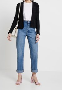 Černý blazer s pruhy přes bílý T-shirt, doplněný o srolované modré džíny a růžové podpatkové sandály. Také je vidět malá bílá kabelka.