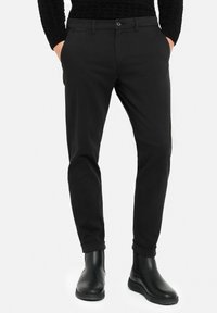 Black tailored trousers made from smooth fabric, featuring a button closure, belt loops, and rolled cuffs, paired with sleek black ankle boots.