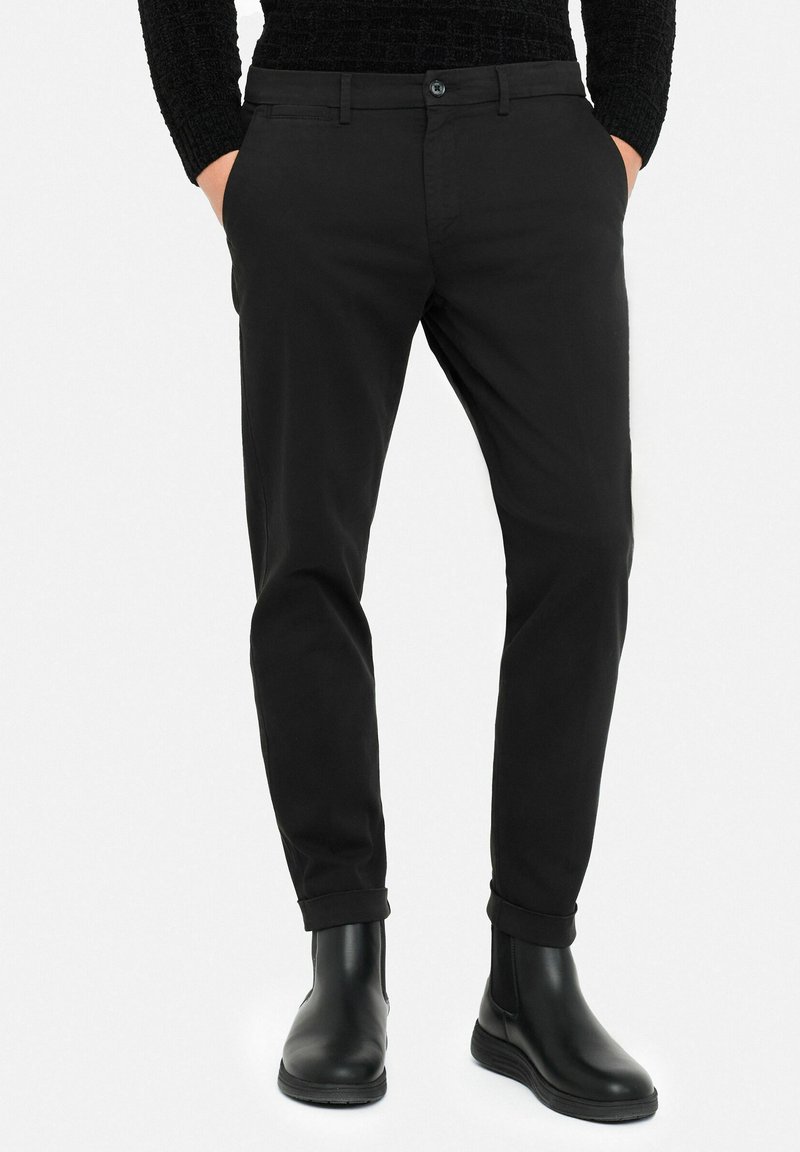 Black tailored trousers made from smooth fabric, featuring a button closure, belt loops, and rolled cuffs, paired with sleek black ankle boots.
