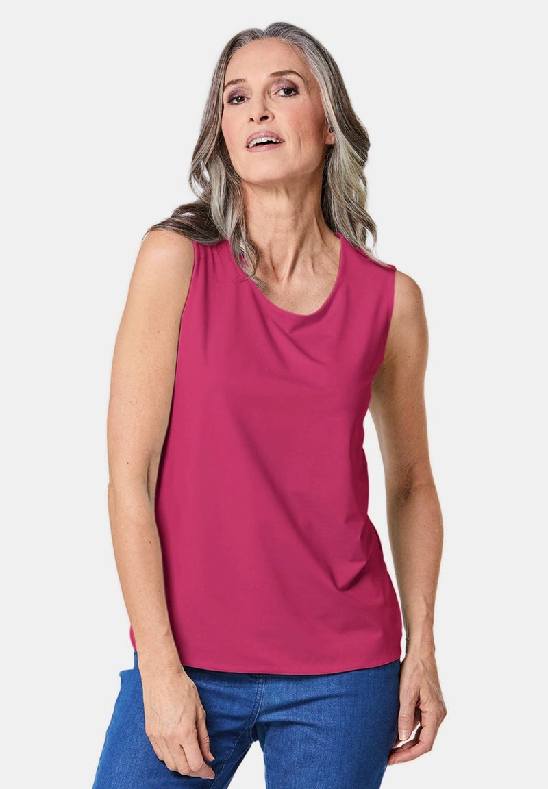 Fuchsia mouwloze top met een ronde hals, gemaakt van gladde stof. Gecombineerd met blauwe jeans poseert het model met één hand op haar heup.