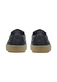 Ein Paar schwarze Leder-Schnürschuhe mit strukturierten beigen Sohlen, von hinten auf einem weißen Hintergrund gezeigt.