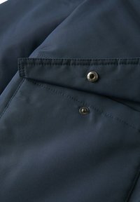 Tissu bleu marine à la texture lisse, doté d'une poche à rabat boutonnée et d'accents métalliques sur le devant.