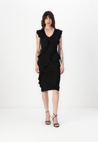 Black dress with ruffle details along the front and shoulders, fitted shape, knee-length, made from smooth fabric. Black strappy heels.
