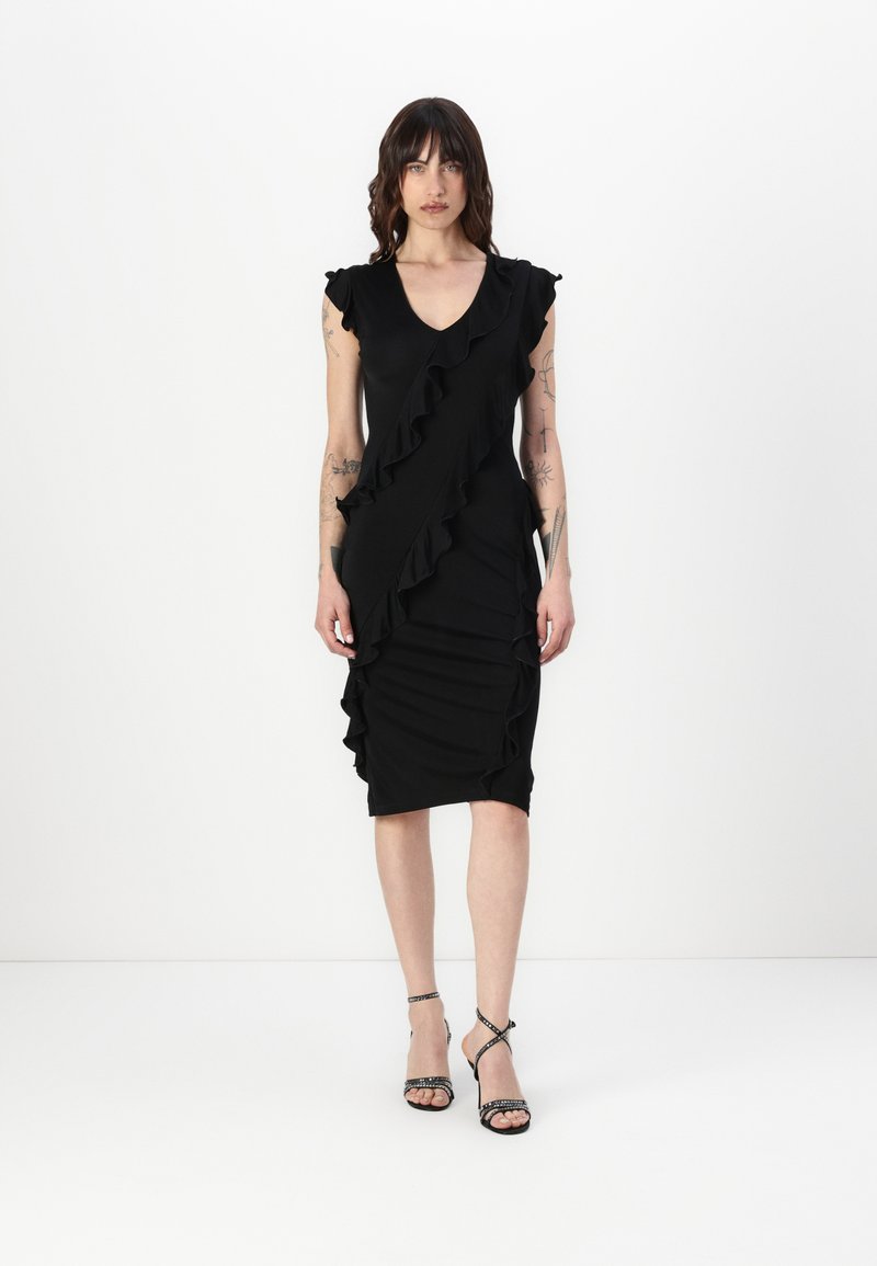 Black dress with ruffle details along the front and shoulders, fitted shape, knee-length, made from smooth fabric. Black strappy heels.