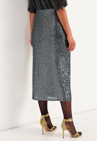 Sprankelende zilveren paillettenrok met een rechte silhouet, knielang, gecombineerd met groene hoge hakken en doorschijnende zwarte panty.