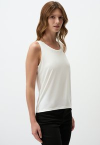 Weißes ärmelloses Tanktop aus weichem Stoff, mit rundem Halsausschnitt und lässiger Passform, kombiniert mit schwarzen Hosen.