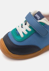 Velcro-Sneaker mit strukturierten Materialien in Blau, Türkis und Marineblau, weißen Schnürsenkeln und einer Gummisohle mit dezentem Profil.
