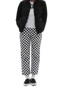 Black jacket over a white t-shirt with "VANS" text. Black and white checkered pants, black slip-on shoes, and white socks with black accents.