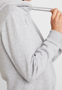 Sweat-shirt à capuche gris avec une texture douce, doté de cordons de serrage et de poignets côtelés. Le tissu semble léger et décontracté.