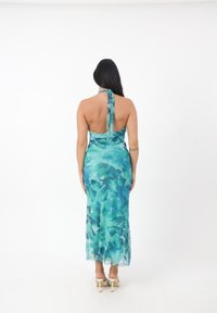 Abito maxi con scollo halter in un motivo floreale gradiente di teal e aqua, con un corpetto aderente e una gonna fluida, dotato di un fiocco sul retro.