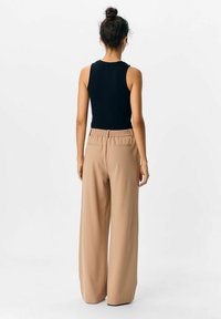 Sort ribbet tanktop parret med brune vidde bukser med elastisk talje og sidelommer, set fra ryggen.