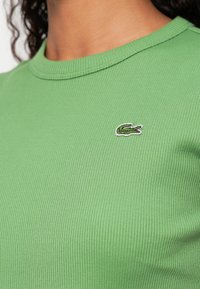 Zielony prążkowany t-shirt z okrągłym dekoltem, z małym, wyszywanym logo krokodyla po lewej stronie.