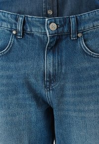 Jeanși din denim de culoare bleu deschis, cu un design clasic cu cinci buzunare, buton metalic cu detalii decorative și cusături.