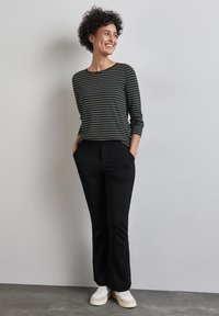 Schwarz-weiß gestreiftes Oberteil mit Dreiviertelärmeln, kombiniert mit schwarzen geraden Hosen und weißen Sneakers. Einfaches Design, lässiger Look.