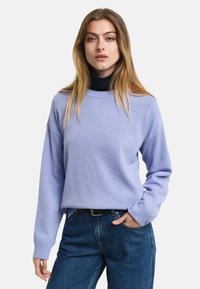 Helles lila Sweatshirt mit langen Ärmeln, geripptem Kragen und lockerem Schnitt, kombiniert mit dunkelblauen Jeans. Weicher Stoff, minimalistisches Design.