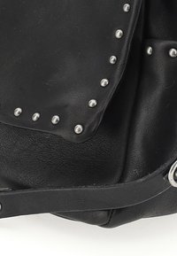 Sac en cuir noir avec des clous argentés le long du rabat. Surface texturée, bandoulière lisse et un détail argenté en forme d'anneau sur le côté.