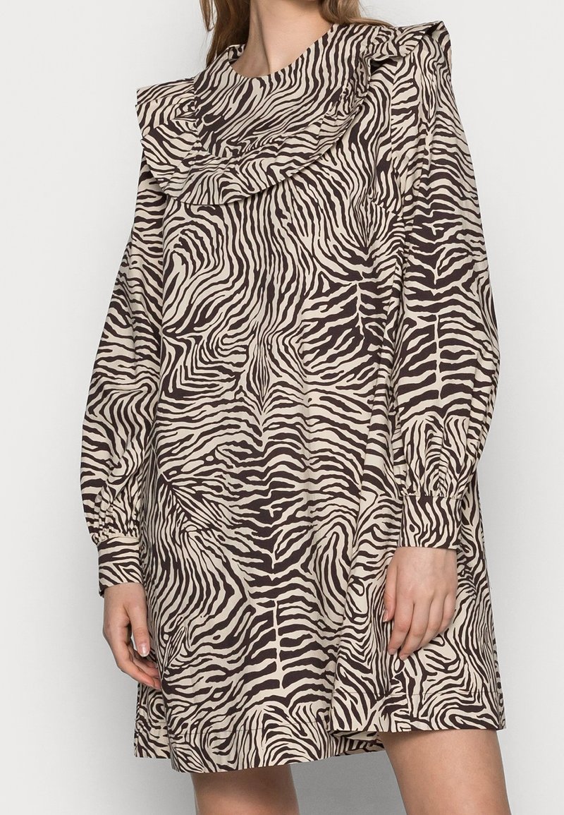 Femme portant une robe à manches longues, longueur genou, avec des rayures zèbre noires et blanches et un grand col volanté.