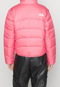 Giacca a vento rosa con sezioni a quadri orizzontali e colletto alto. Logo sulla spalla sinistra. Abbinata a pantaloni in similpelle nera.
