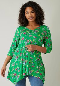 Grüne Tunika mit floralem Muster in Pink, Blau und Gelb. V-Ausschnitt, drei Viertelärmel und asymmetrischer Saum. Weicher Stoff.