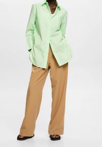 Camicia button-up verde chiaro con maniche lunghe, abbinata a pantaloni larghi color beige. L'outfit presenta una vestibilità rilassata e una texture del tessuto morbida.