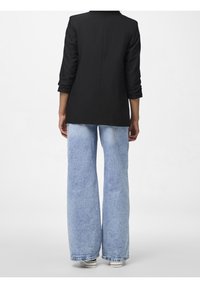 Blazer noir à coupe ajustée avec manches trois-quarts, associé à un jean large bleu clair présentant une texture en denim délavé.