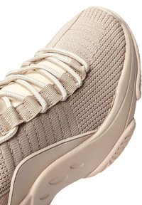 Beige sneaker featuring a textured knit upper, flat laces, and a smooth rubber sole with circular tread patterns.