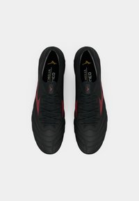 Um par de sapatilhas desportivas pretas com detalhes em vermelho, atadas, vistas de cima sobre um fundo branco.
