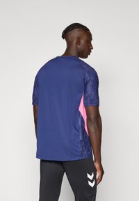 T-shirt de sport bleu marine avec un motif texturé sur les manches, avec des panneaux latéraux roses. Design à manches courtes et col rond.