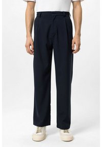 Marineblauwe plisségordelbroek gemaakt van een gladde stof, met een getailleerde pasvorm, zijzakken, en gedragen met lichtgekleurde sneakers.