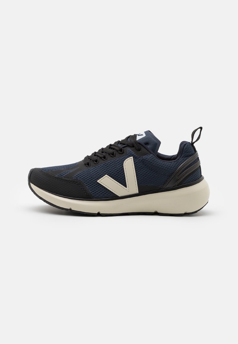 Baskets de sport bleu foncé et noir avec semelle épaisse beige, lacets à l'avant, logo latéral et languette au talon sur fond blanc.