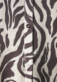 Lyhythihainen paita, jossa on beige ja ruskea zebra-kuvio, napitus edessä ja kontrastiväri päällä. Joustava kangas.