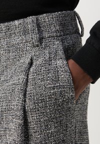 Pantaloni grigi e neri mélange in misto lana con motivo a fantasia, fronte piatto, tasche laterali e vestibilità sartoriale, con passante per cintura e tessuto strutturato.