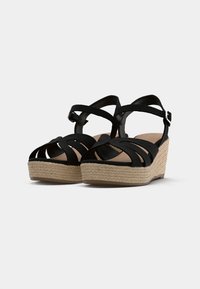 Sandales compensées noires avec une semelle intermédiaire en jute tressé, dotées de brides entrecroisées et d'une bride réglable à la cheville pour un maintien sécurisé.