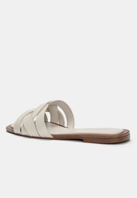 Sandales à glissière beige clair avec un design à lanières, fabriquées en matériau lisse, dotées d'une semelle plate et d'un bout arrondi. Détails de couture subtils visibles.