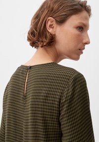 Grünes und schwarzes Karomuster-Oberteil mit rundem Ausschnitt, einem Rückenschlitz mit Knopfdetail und weichem Stoff mit strukturiertem Muster.