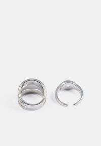 Sølv ring sæt, der består af en tykkeband med en struktureret overflade og en mindre åben ring med en lille fordybning. Glat finish.