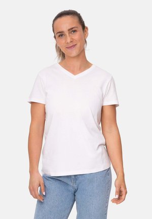 T-shirt bianca in cotone con maniche corte e scollo a V, caratterizzata da una vestibilità comoda. Il modello indossa jeans di denim azzurro chiaro.