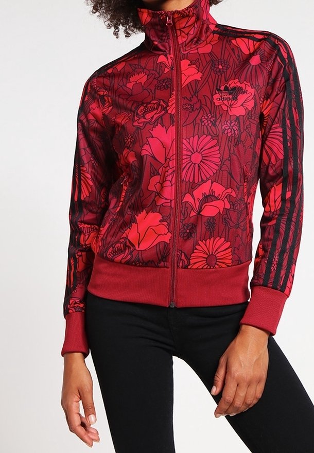 Czerwona kurtka zapinana na zamek z kwiatowym wzorem w odcieniach różu i czerni, z czarnymi paskami na rękawach oraz ściągaczami.