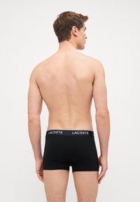 Czarne bokserki wykonane z miękkiego materiału, z jednolitym wzorem i elastycznym pasem w talii, na którym z przodu znajduje się białe logo "LACOSTE".