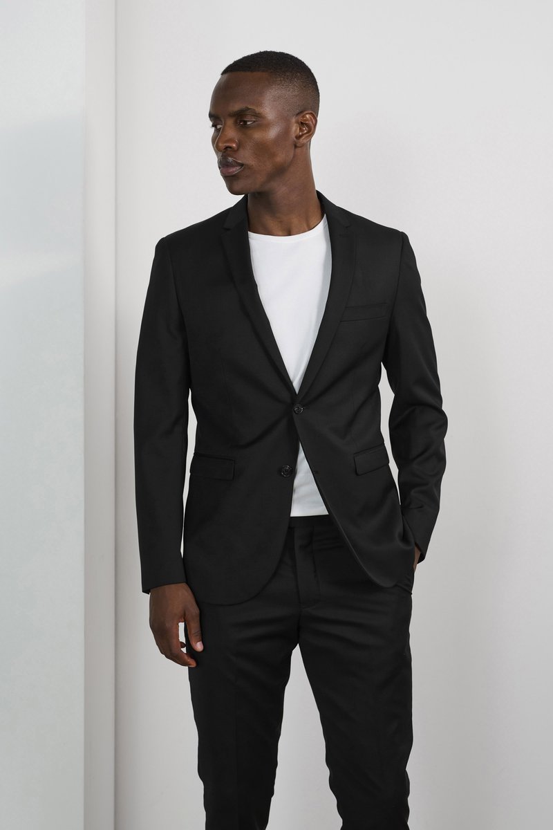 Giacca nera fitted con chiusura a un solo bottone, abbinata a una t-shirt bianca a collo rotondo, pantaloni neri slim e texture del tessuto liscia.