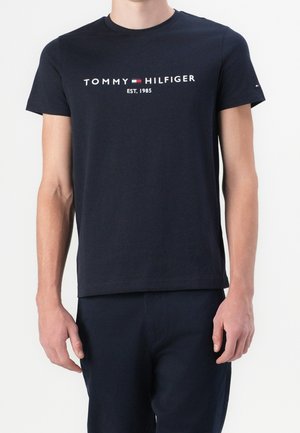 T-shirt en coton bleu marine à manches courtes, col rond, avec l'inscription blanche "TOMMY HILFIGER EST. 1985" sur la poitrine. Design minimaliste.