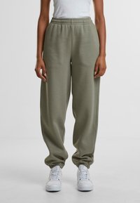 Grønne joggebukser laget av mykt materiale med elastisk midje, med en avslappet passform og avsmalnede mansjetter, paret med hvite joggesko.