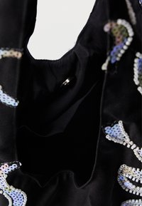 Μαύρη υφασμάτινη τσάντα με εσωτερικό κυκλικό στύλο; διακοσμημένη με ιριδίζουσες παγιέτες που σχηματίζουν ένα σχέδιο κατά μήκος της άκρης. Λείο υλικό.